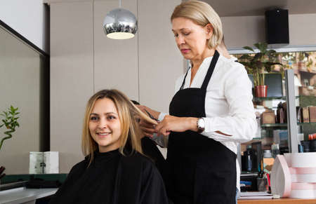 Woman in a black apron parkmaher cuts the young woman at the hairdresser salonの写真素材