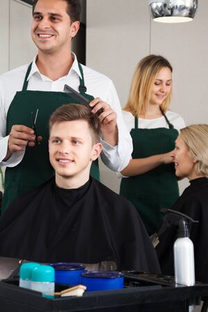 Positive male hairstyler serving teenager in hair of salonの写真素材