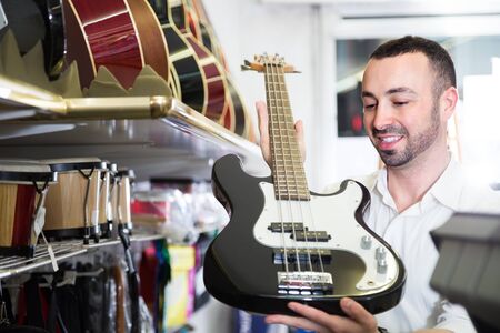Young customer choosing new guitar in shop and smilingの写真素材