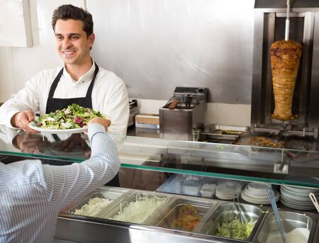 portrait of a young male fast food worker at counter of kebab cafeの写真素材