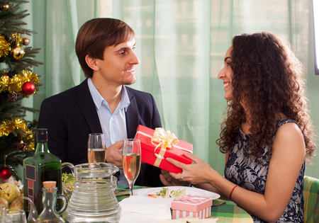 Woman presenting gift to man at table during  dinner at homeの写真素材