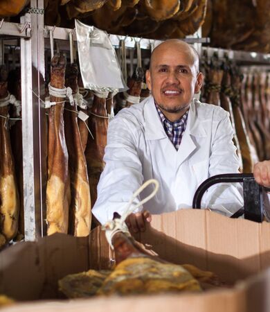 Worker in white gown checking joints of iberico jamon at factoryの写真素材