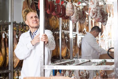 Mature Worker in white gown checking joints of iberico jamonの写真素材
