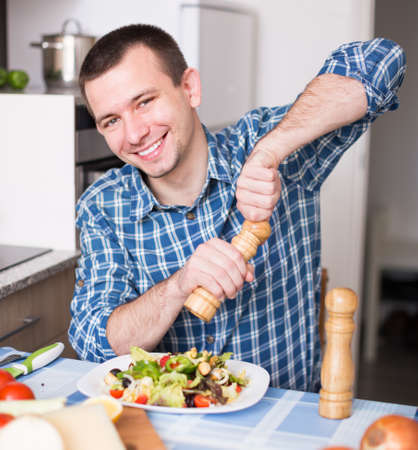 smiling man adding spice to the saladの写真素材
