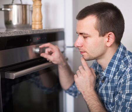 ordinary man controls the oven in the kitchenの写真素材