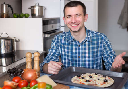 Young smiling man preparing pizza in the kitchen at homeの写真素材