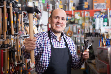 Mature male seller offering hammer in household storeの写真素材