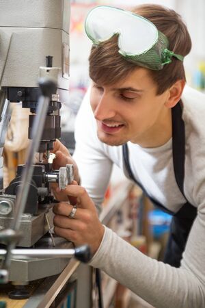 Young ordinary handyman making door keys copies in locksmith