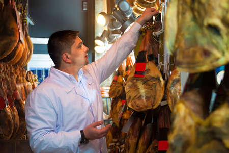 Midle aged butcher checking drying wurst and jamon at factory