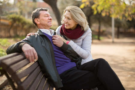 Mature family couple on a bench in the park in autumn day and smilingの写真素材