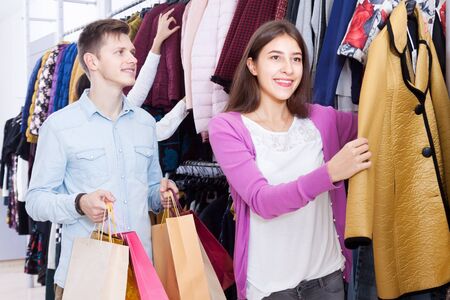 A young couple in a clothing store. A woman holding a coatの写真素材