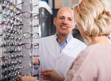 Professional male optician consulting mature blonde customer  spectacles at the displayの写真素材