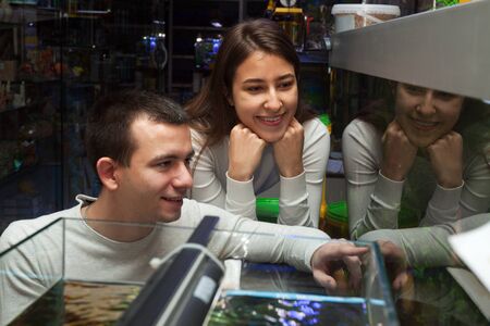 Young guy and girl smiling and watching aquarium fish in aquarium in storeの写真素材