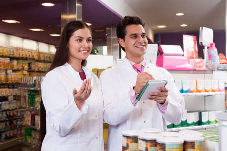 Sellers at the pharmacy. Smiling woman and a man with a notebook in the hands of a white coat.の写真素材