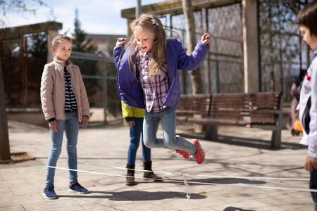 children games. blonde Girl jumps over the rope in the yard in springの写真素材