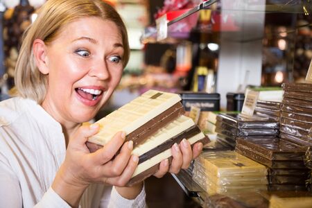 Happy blonde pensioner buying dark and white chocolate filled candiesの写真素材