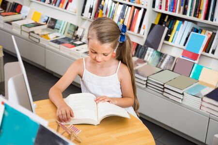 little smart girl reading a book in the school library