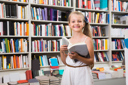 smiling nice blonde girl chooses a book in the libraryの写真素材