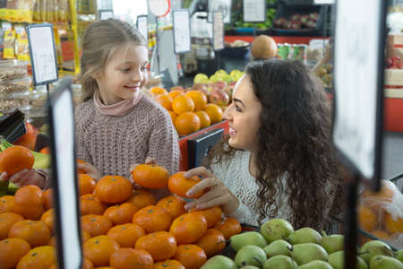 mother and blonde daughter buying mandarins in shopの写真素材