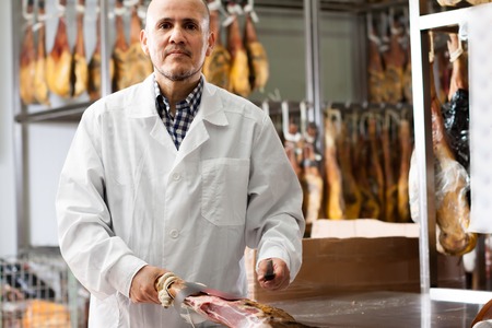 Mature butcher slicing jamon and in delicatessen storeの写真素材