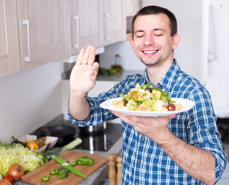 young guy posing with a plate of gourmet salad in the kitchenの写真素材