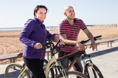 middle-aged  man and a woman with bicycles walking on the beachの写真素材