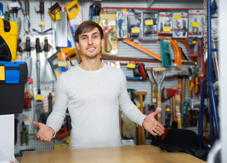 Young positive male seller posing at tooling section of household storeの写真素材