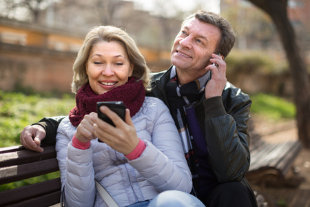 Senor man and woman with mobile phones in sunny spring dayの写真素材