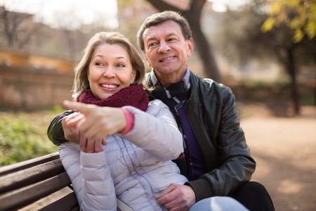 Happy elderly family couple on a bench in the park in autumn dayの写真素材