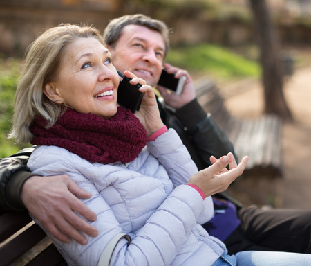 elderly couple talking on the phone on a park bench in spring dayの写真素材