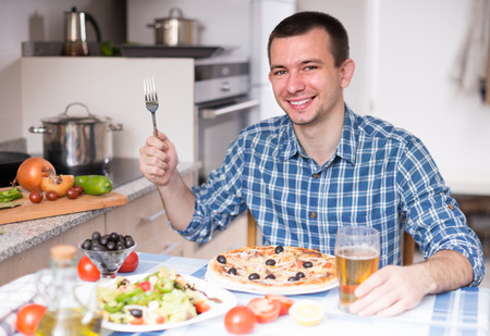 single guy eating pizza and salad in the kitchen at homeの写真素材