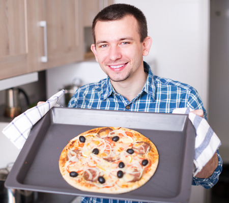 happy young man holding baking sheet with delicious pizzaの写真素材