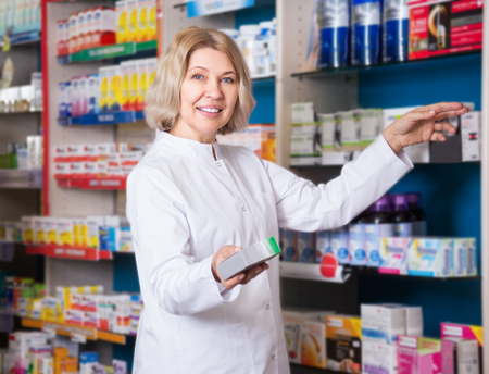 Smiling mature female pharmacist posing in drugstoreの写真素材