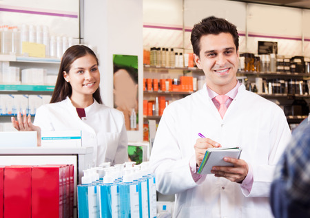 Pharmacist man writes in a notebook. Woman pharmacist smilingの写真素材