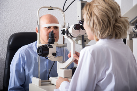 Eldery optician examinating male eyesight with aid of slit lampの写真素材