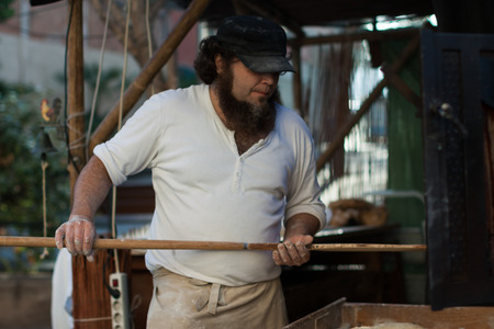 Man is going to take out the bread out of the oven a wooden shovel