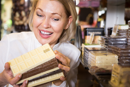 
Happy blonde pensioner buying dark and white chocolate in cafeの写真素材