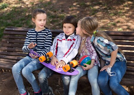 Happy girl and boy sitting and whispering in the park on bench inpark in springの写真素材