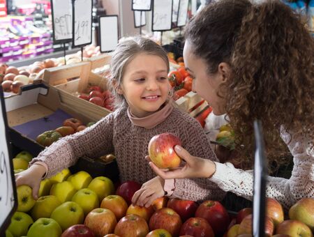 mother and smiling daughter buying apples in shopの写真素材