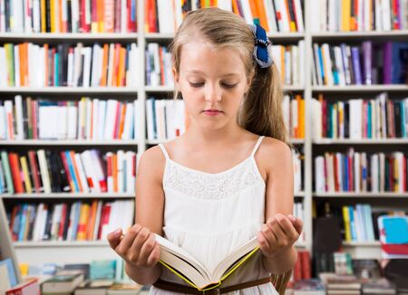 beautiful girl child considers the book in a bookstoreの写真素材