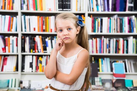 pensive blond girl child puzzled of selection of books in the storeの写真素材