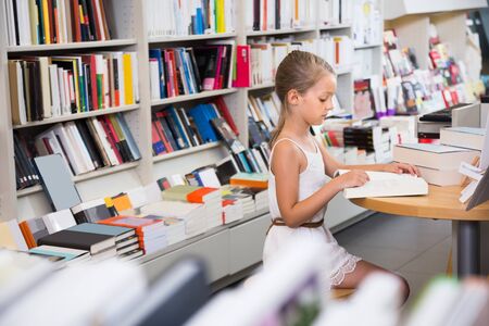 studious smart girl child is engaged with a book in the libraryの写真素材