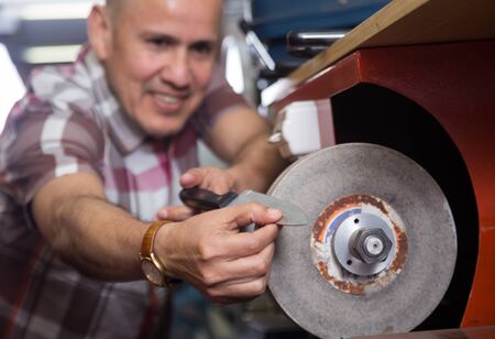 Senior workman resharpering knives on interlock spiral wheel system machine. Fokus on knife.