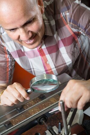 mature smiling man looking through a magnifying glass on a item