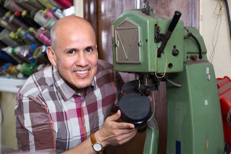 Professional positive shoemaker stitching footwear on machine in shoe atelierの写真素材