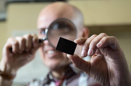 mature man looking through a magnifying glass on a itemの写真素材