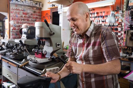 positive Elderly specialist stitching shoes on leather sewing machine at factory 