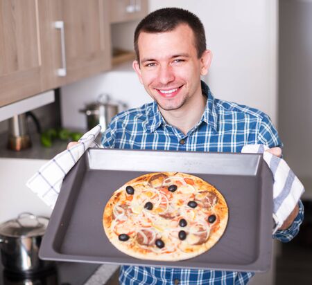 young man holding baking sheet with delicious pizza and smilingの写真素材