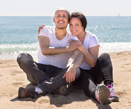 smiling mature man and female sitting near seaの写真素材