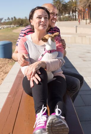mature man with a woman sitting on bench with dog in springの写真素材